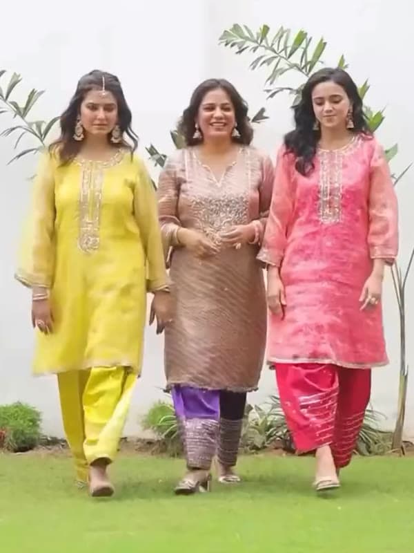 Three women walking through a garden in yellow, gold and pink kurta sets